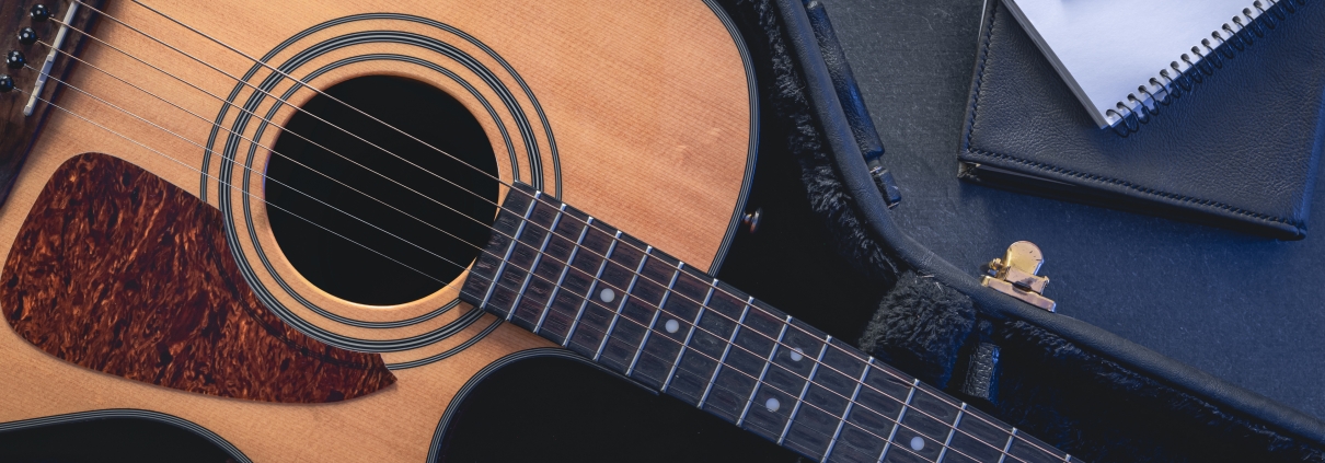 Acoustic guitar and notepad with pencil, top view.